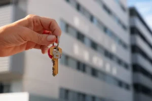 Imagen de una mano sosteniendo unas llaves en frente de un edicio residencial